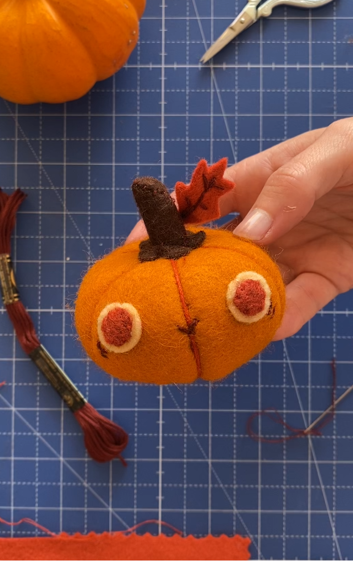 mini citrouille en feutrine kawaii. Sur un tapis bleu de création avec ciseaux et fil DMC et aiguille et feutrine.